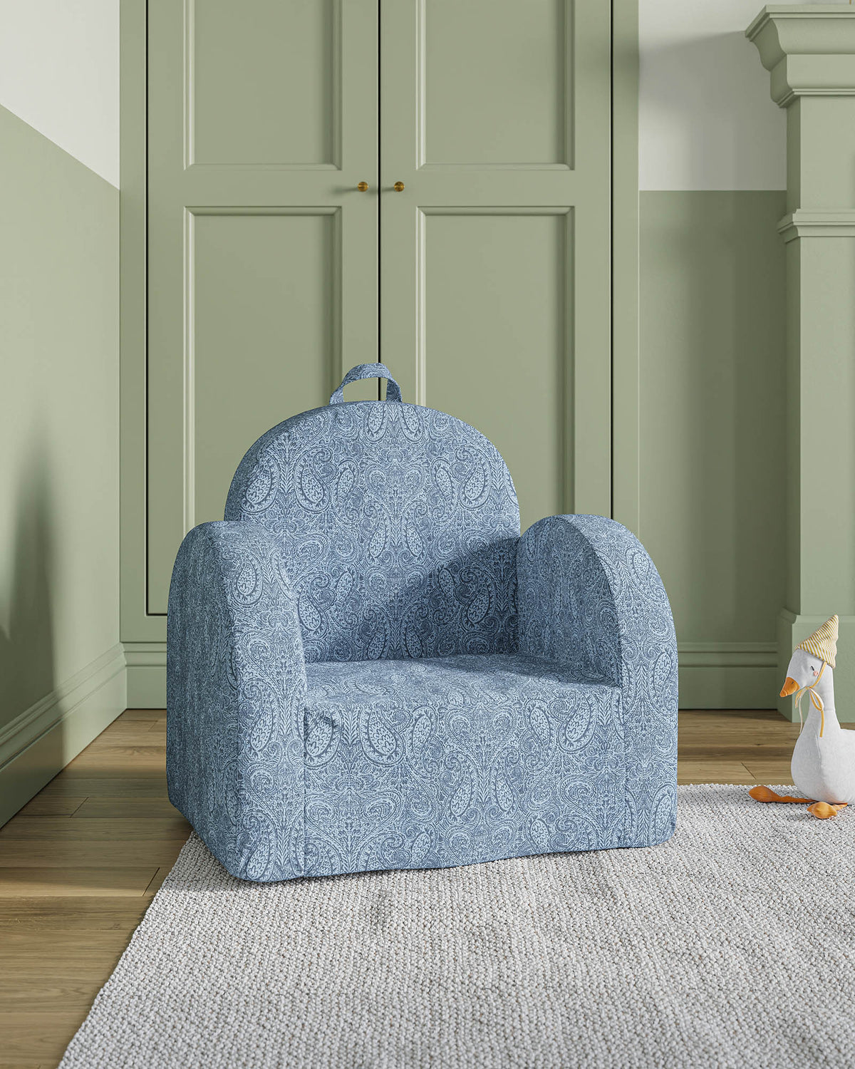 Small armchair with a white fabric featuring colorful vegetables and animals, in a room with green walls.